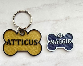 May include: Two dog bone-shaped name tags, one yellow with the name "ATTICUS" and one blue with the name "MAGGIE".