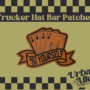 May include: A tan Trucker Hat Bar Patch with a design of three playing cards with the Ace of Spades, Clubs, and Diamonds. The patch has the words "BET ON YOURSELF" on a banner. The background is olive green.