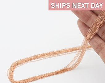May include: A close-up of a rose gold chain necklace. The chain is delicate and has a fine, smooth finish. The chain is laid out in a loop, with multiple strands of the chain visible.