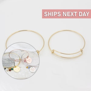 May include: Two gold expandable bangle bracelets with a charm attached to each. The charms are round and have different engraved messages. One charm says "Sweet 16." The other charm says "You're the perfect wife for me."