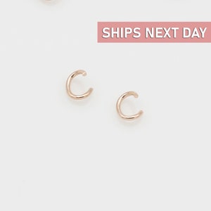 May include: A pair of gold ear cuffs. The ear cuffs are made of a thin, round wire and are designed to sit on the upper part of the ear.