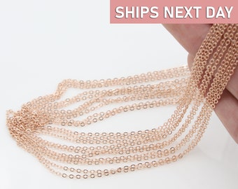May include: A close-up of a rose gold chain necklace. The chain is made of small, delicate links. The chain is shown in a hand, with the text "SHIPS NEXT DAY" in the background.