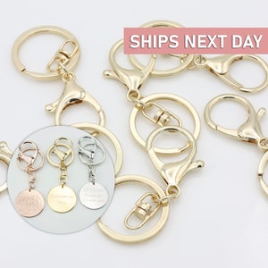 May include: Gold keychains with a lobster clasp and a split ring. Three keychains have round metal tags with different engravings: "Mama Bear", "Customize This", and "If Found Please Call 123-456-7890".