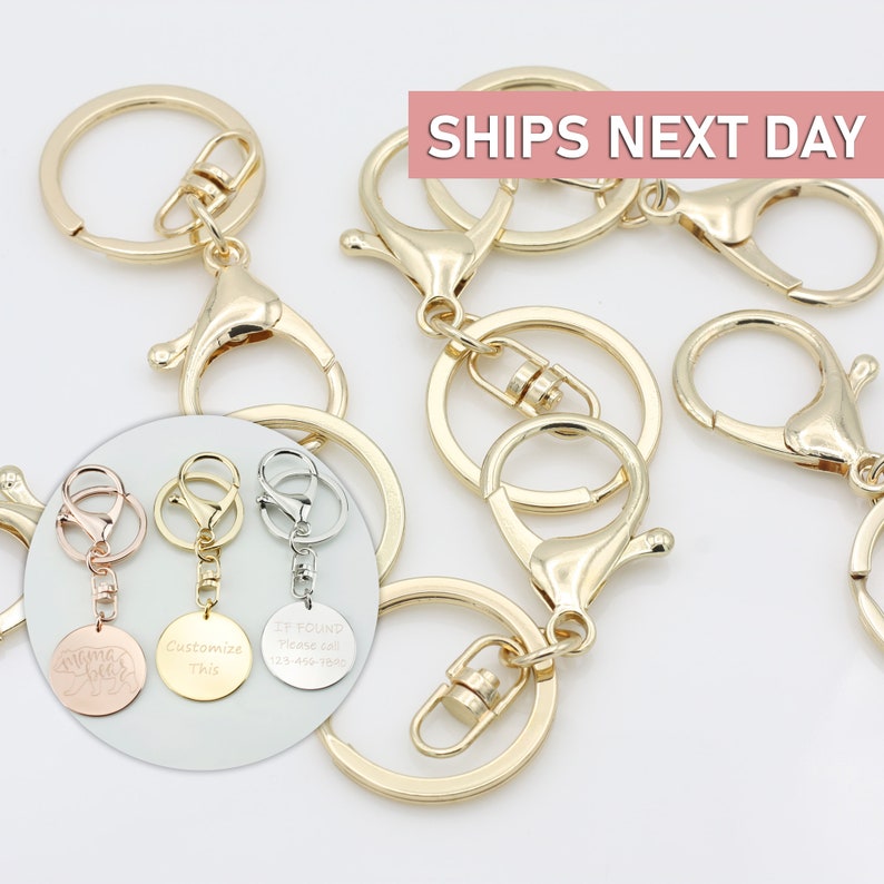 May include: Gold keychains with a lobster clasp and a split ring. Three keychains have round metal tags with different engravings: "Mama Bear", "Customize This", and "If Found Please Call 123-456-7890".