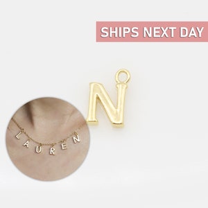 May include: Gold letter N charm pendant. The charm is shown on a necklace with the name LAUREN spelled out in gold letters.