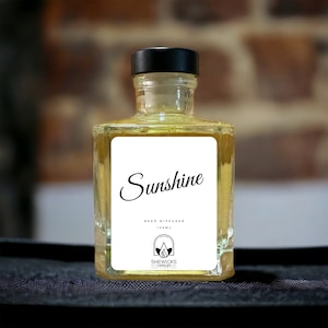 Op de afbeelding: Een vierkante glazen fles voor een geurstokjesverspreider gevuld met gele vloeistof, met een zwarte dop en een wit etiket. Het etiket bevat de tekst Sunshine, REED DIFFUSER, 125 ML en een logo met de tekst SHEWICKS CANDLES MADE IN NEW YORK.