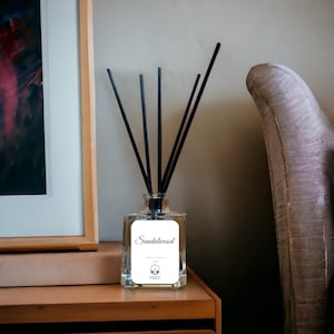 Può includere: Un diffusore a bastoncini in vetro trasparente con un'etichetta rettangolare bianca che riporta il testo Sandalwood, Reed Diffuser, 100ml e un piccolo logo. Cinque sottili bastoncini neri sono inseriti nel flacone dal collo stretto.