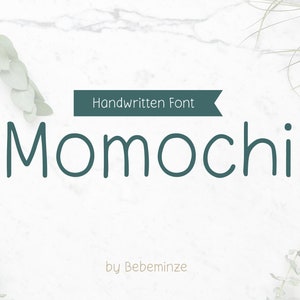 Può includere: Font tipografico scritto a mano chiamato "Momochi" di Bebeminze, mostrato su uno sfondo di marmo bianco con vegetazione verde.