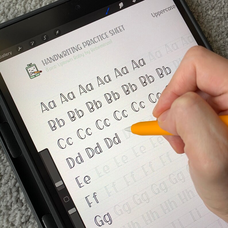 May include: A digital tablet screen displaying a handwriting practice sheet with uppercase letters from A to I. The sheet is titled "Handwriting Practice Sheet" with the font name "Uptown Baby by Rebeminze". A hand is holding a stylus and tracing over the letter "D".