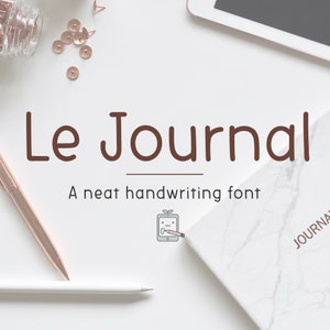 Może przedstawiać: Białe tło z brązowym ręcznie pisanym fontem, który mówi "Le Journal" i "A neat handwriting font". Jest mała ilustracja tabletu z ołówkiem i rośliną na nim. Jest biały marmurowy notes z napisem "JOURNAL" na nim.