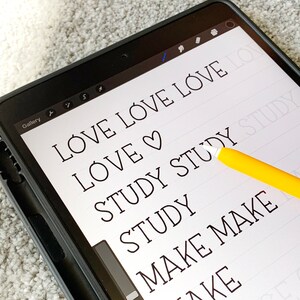 May include: A digital tablet screen displaying the words "LOVE LOVE LOVE", "LOVE", "STUDY STUDY STUDY", "STUDY", "MAKE MAKE", and "KE" written in a handwritten font. A yellow stylus is resting on the screen.