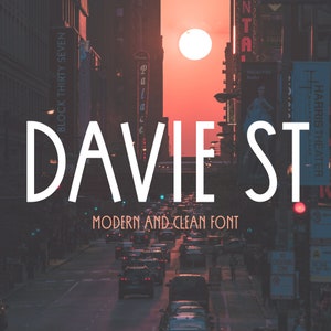 May include: A city street scene at sunset with the text "DAVIE ST" in a modern, clean font. The text is centered on the image and is in white against a dark background. The street is lined with buildings and cars.