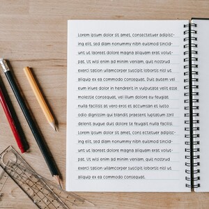 Puede incluir: Un cuaderno espiral abierto, con p&aacute;ginas rayadas, lleno del texto "Lorem ipsum dolor sit amet...", est&aacute; junto a tres l&aacute;pices y una regla transparente sobre una superficie de madera. Los l&aacute;pices son rojo, negro y amarillo.