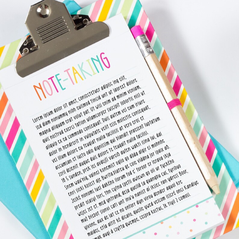 May include: A white clipboard with the words "NOTE-TAKING" in colorful letters at the top. The clipboard has lined paper and a pink pencil is sticking out of the top.