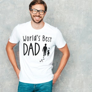 May include: White t-shirt with the text "World's Best Dad" and a silhouette of a father and child walking with hearts.