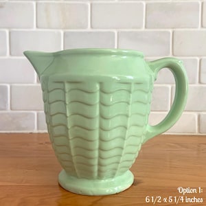 May include: A pale green ceramic jug with a handle and spout. The jug features a textured, woven-style pattern on the body. It measures approximately 16.5 x 13.3 cm.