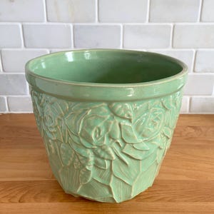 May include: A green ceramic planter with a floral design. The planter is embossed with a pattern of roses and leaves.