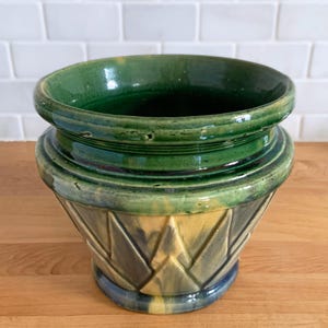 May include: A green and yellow glazed ceramic planter with a geometric pattern. The planter has a wide rim and a rounded base.