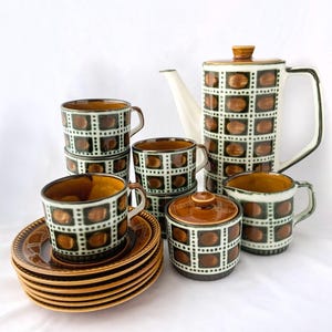 May include: A vintage tea set with a brown and green geometric pattern. The set includes a teapot, creamer, sugar bowl, and four cups and saucers.