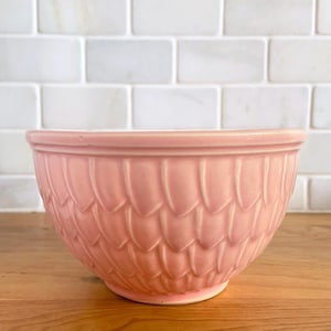 May include: A pink ceramic mixing bowl with a scalloped design. The bowl is round and has a smooth, glossy finish.
