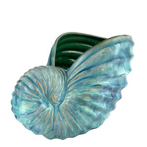 May include: A ceramic nautilus shell-shaped decorative bowl. The bowl has a swirling design in shades of blue, teal, and gold. The interior is a deep green colour. The shell is a decorative item.