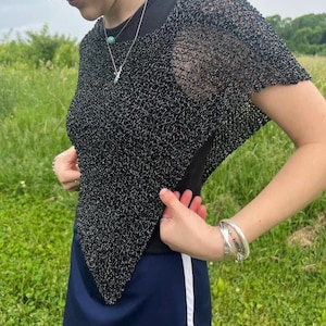 May include: A black short-sleeved top featuring a metallic silver open-knit mesh texture with a pointed hemline, worn over a solid black base layer, paired with a dark blue skirt that has a white vertical stripe along the side seam.