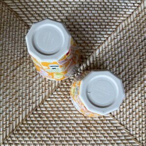 Puede incluir: Dos tazas de cer&aacute;mica con un vibrante estampado floral en amarillo, rojo y verde. Las tazas tienen una forma octogonal &uacute;nica y una base blanca. Las tazas est&aacute;n colocadas sobre una superficie tejida.