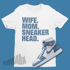 May include: White t-shirt with the text "Wife. Mom. Sneaker Head." in blue lettering. A pair of blue and white sneakers are shown on the bottom right of the image.