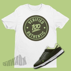 Puede incluir: Camiseta blanca con un logotipo circular verde que dice "Verified 100 Authentic". Un par de zapatillas verdes y negras con un logotipo swoosh blanco.