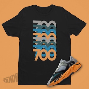 May include: Black t-shirt with a graphic of the number 700 repeated in different colors. A pair of orange and grey sneakers with a black sole are in the bottom right corner of the image.