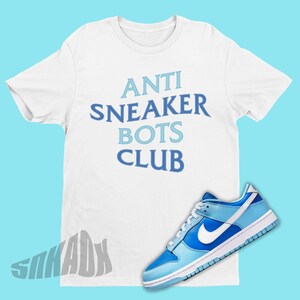 May include: White t-shirt with the text "ANTI  SNEAKER BOTS CLUB" in blue and light blue lettering. A pair of light blue and white Nike sneakers are on the bottom right of the image.