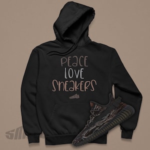 May include: Black hoodie with the text "peace love sneakers" in brown and white lettering. A pair of black and brown sneakers are in the bottom right corner of the image.
