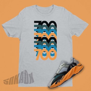 Peut inclure: Un t-shirt gris avec le nombre 700 r&eacute;p&eacute;t&eacute; dans un design empil&eacute; dans des tons de bleu, vert et orange. Une paire de baskets grises, vertes et orange avec un motif de flamme sur la semelle.