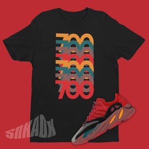 Puede incluir: Camiseta negra con un gr&aacute;fico del n&uacute;mero 700 repetido en diferentes colores. Un par de zapatillas rojas, negras y amarillas se muestra en la parte inferior derecha de la imagen.