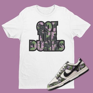 May include: White t-shirt with the text "GOT THE DUNKS" in black with a floral pattern. A pair of white and black sneakers with a floral pattern.