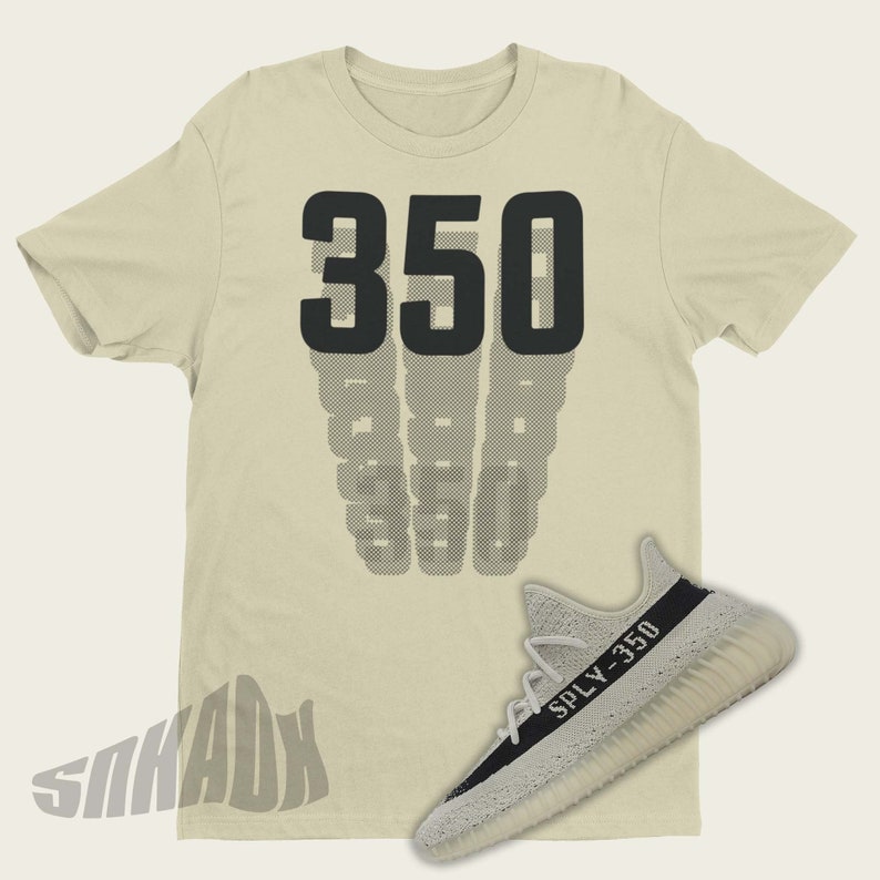 May include: A beige t-shirt with the number 350 printed on the front. The shirt is paired with a pair of white and black sneakers with the text "SPLY-350" on the side.