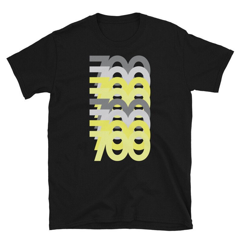 Op de afbeelding: Zwart T-shirt met een grafisch ontwerp van het getal 700 in geel en grijs. Het getal is gelaagd en gestapeld op zichzelf.