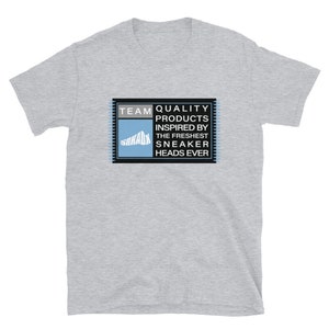 K&ouml;nnte beinhalten: Graues T-Shirt mit einer rechteckigen Grafik in Schwarz und Blau, auf der "TEAM QUALITY PRODUCTS INSPIRED BY THE FRESHEST SNEAKER HEADS EVER" steht.