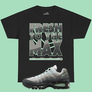 May include: A black short-sleeve t-shirt featuring the text FRESH TO THE MAX in large block letters with a layered gray and mint green graphic design. Below the text is a horizontal gauge labeled LOW, MEDIUM, HIGH, MAX. A gray and mint sneaker is below.
