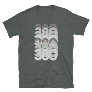 May include: A dark heather grey t-shirt with a graphic design of the number 380 repeated in a layered, faded effect. The numbers are in a light grey color.