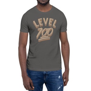 May include: A dark grey t-shirt with the text "LEVEL 100" in a brown and beige colour scheme. The text is in a retro, stylised font.