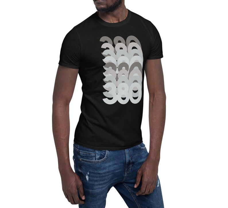 Puede incluir: Una camiseta negra de manga corta con un dise&ntilde;o gr&aacute;fico del n&uacute;mero 380 repetido en un patr&oacute;n superpuesto en capas en tonos grises.