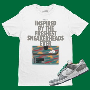 May include: White t-shirt with the text "Inspired by the Freshest Sneakerheads Ever" and a small box with a colorful abstract design. A white and grey sneaker with green accents is in the bottom right corner.