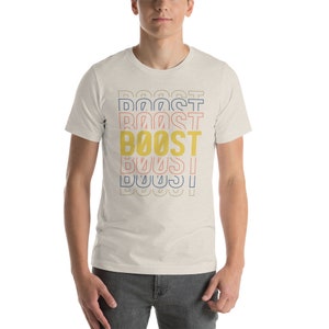 May include: A white t-shirt with a graphic design of the word "BOOST" repeated in different colors and sizes. The word "BOOST" is in yellow, with blue and pink outlines.
