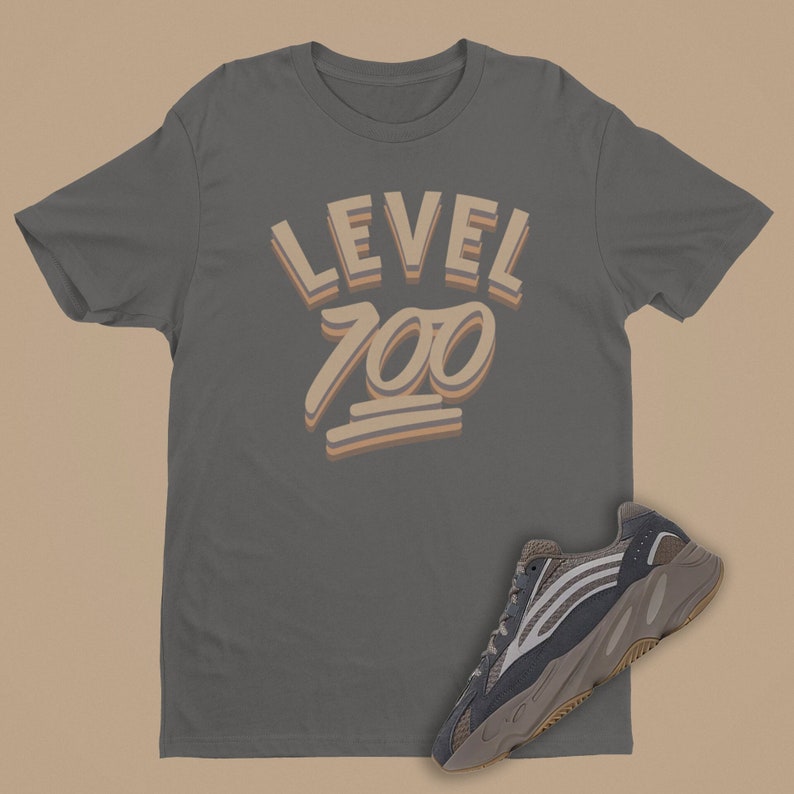May include: A grey t-shirt with the text "LEVEL 700" in a retro font. The shirt is paired with a grey and white trainer with a thick sole.
