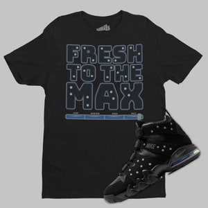 May include: Black t-shirt with the text "FRESH TO THE MAX" in blue with white dots. A black Nike Air Max Uptempo basketball shoe with white dots and a blue swoosh is on the bottom right of the image.