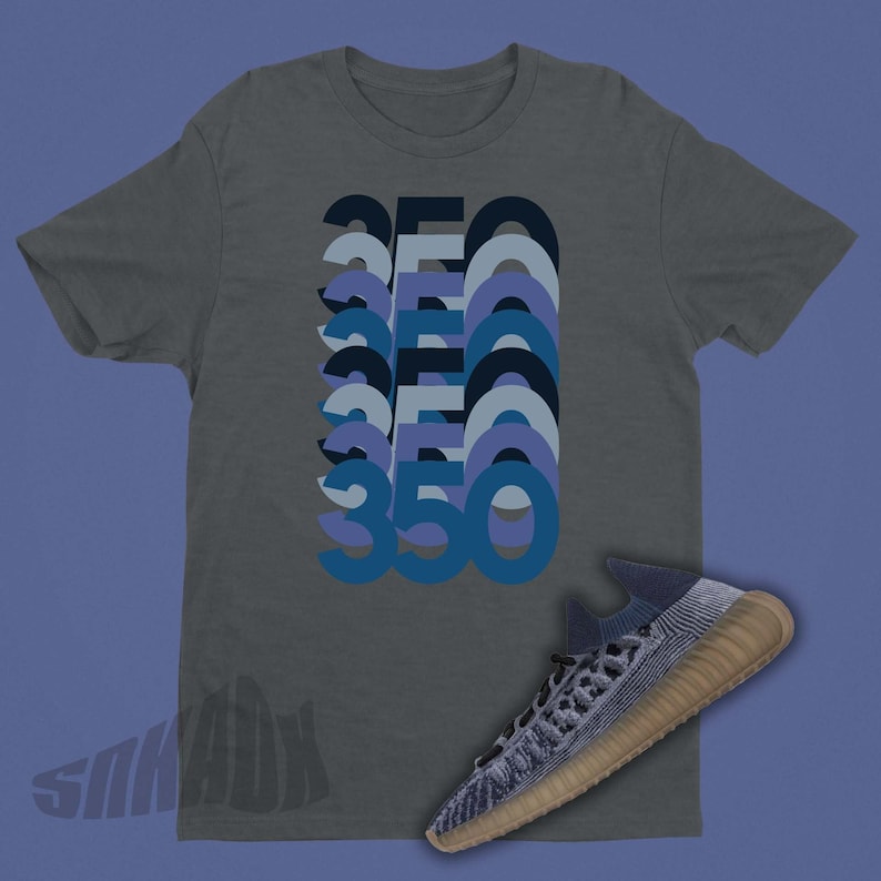Peut inclure: Un t-shirt gris fonc&eacute; avec un motif repr&eacute;sentant le nombre 350 r&eacute;p&eacute;t&eacute; dans un design superpos&eacute; et en couches dans des tons de bleu. Une chaussure en maille bleue et grise avec une semelle beige est repr&eacute;sent&eacute;e sous le t-shirt.
