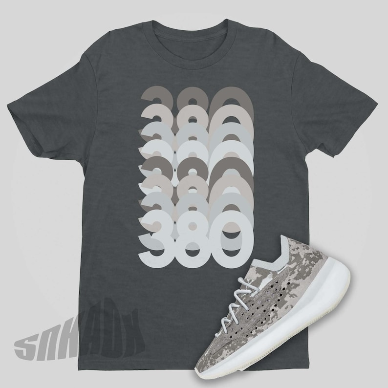 May include: A dark gray t-shirt with a graphic of the number 380 repeated in different shades of gray. A white and gray camouflage sneaker is also pictured.