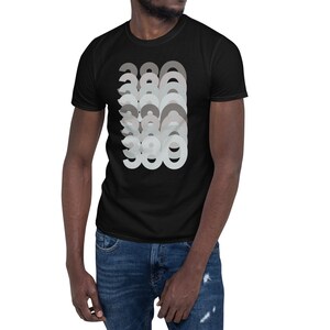 Puede incluir: Camiseta negra con un dise&ntilde;o gr&aacute;fico del n&uacute;mero 380 repetido en un patr&oacute;n superpuesto en capas de diferentes tonos de gris.