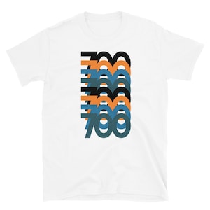 May include: White t-shirt featuring a graphic design of the number 700 repeated in a stacked pattern. The numbers are in black, orange, and blue.